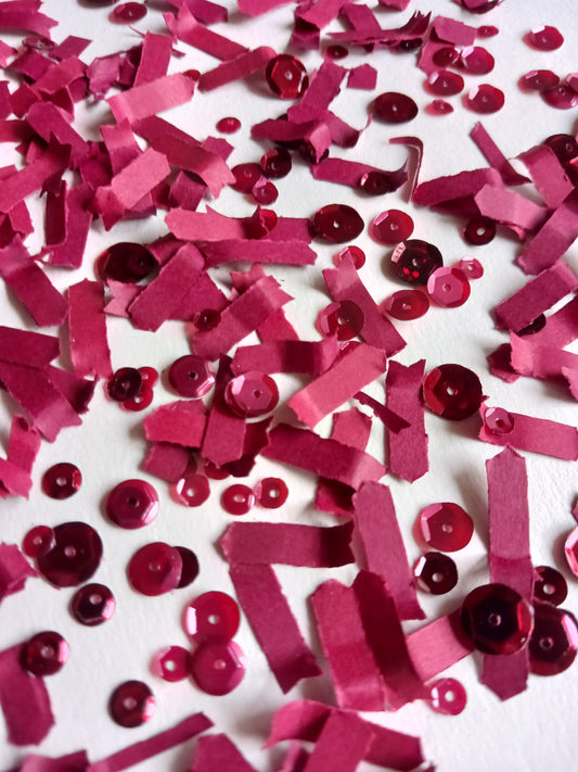 Wine red paper confetti and red sequins on white background.