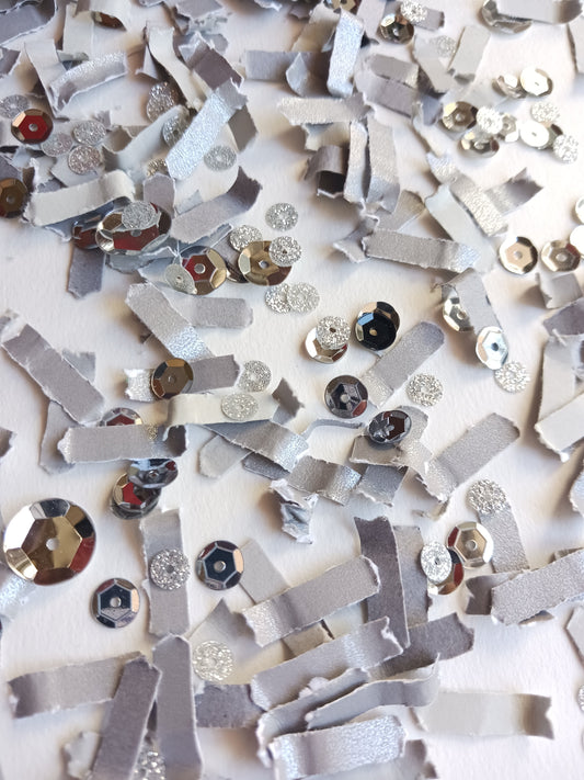 Silver paper confetti with silver sequins on white background.