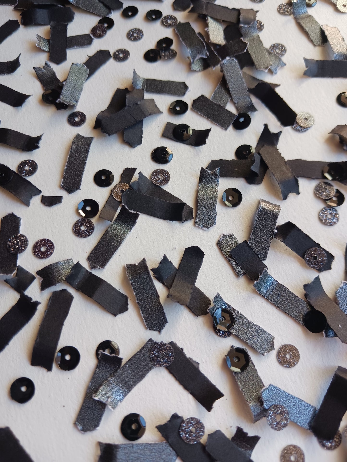 Scattered black confetti with black sequins on a white background.