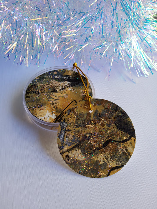 Black and gold glitter abstract hand-painted round gift tags with gold cords in a round acrylic container and iridescent tinsel background