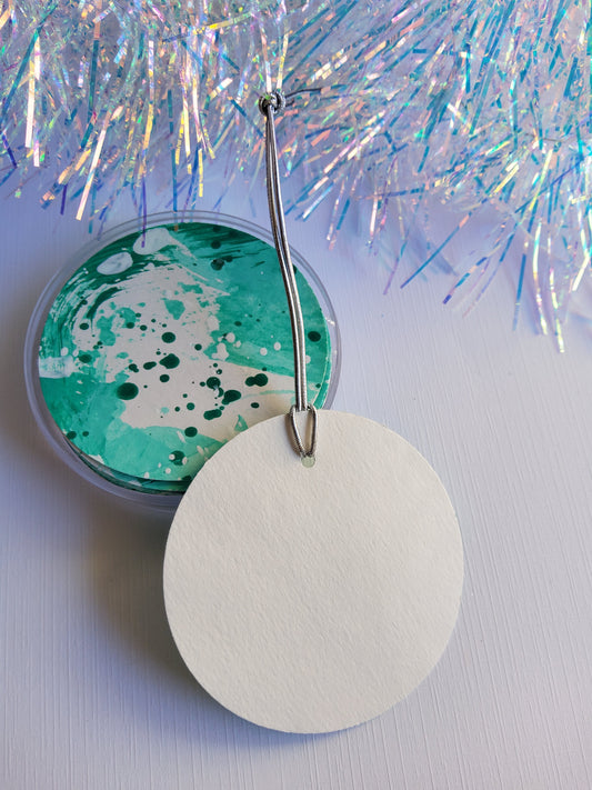 Set of jade green hand-painted abstract gift tags with silver stretch cords displayed beside iridescent tinsel on white background