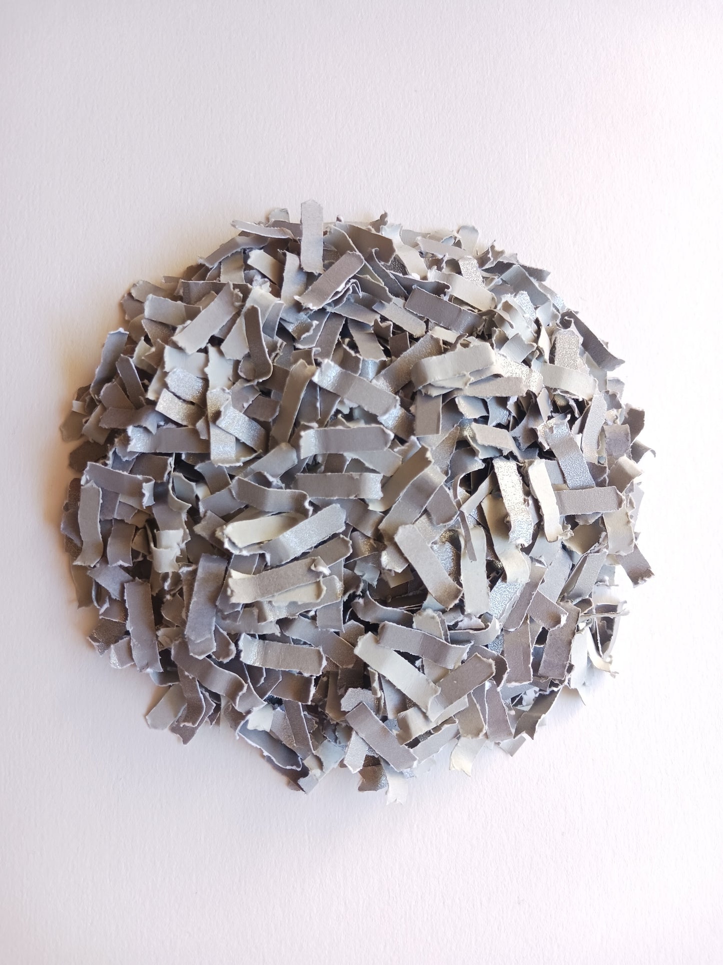 Silver grey shimmer paper confetti in a round pile on white background.