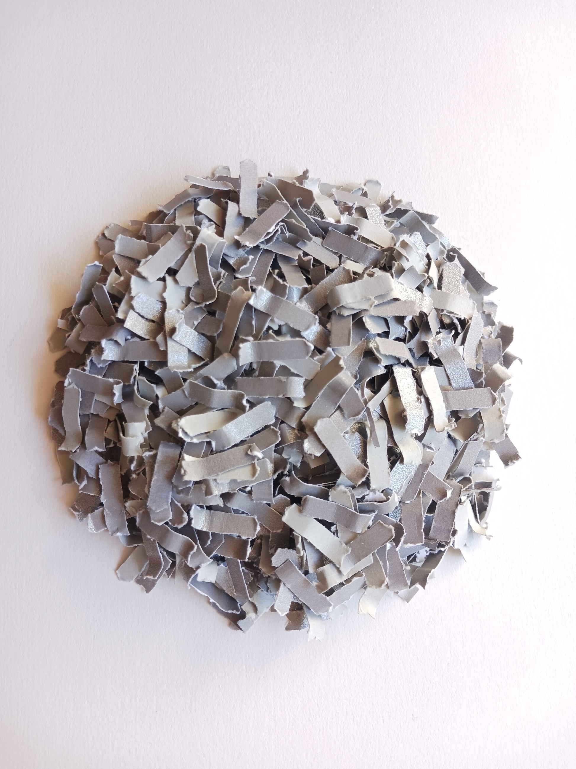 Silver grey shimmer paper confetti in a round pile on white background.