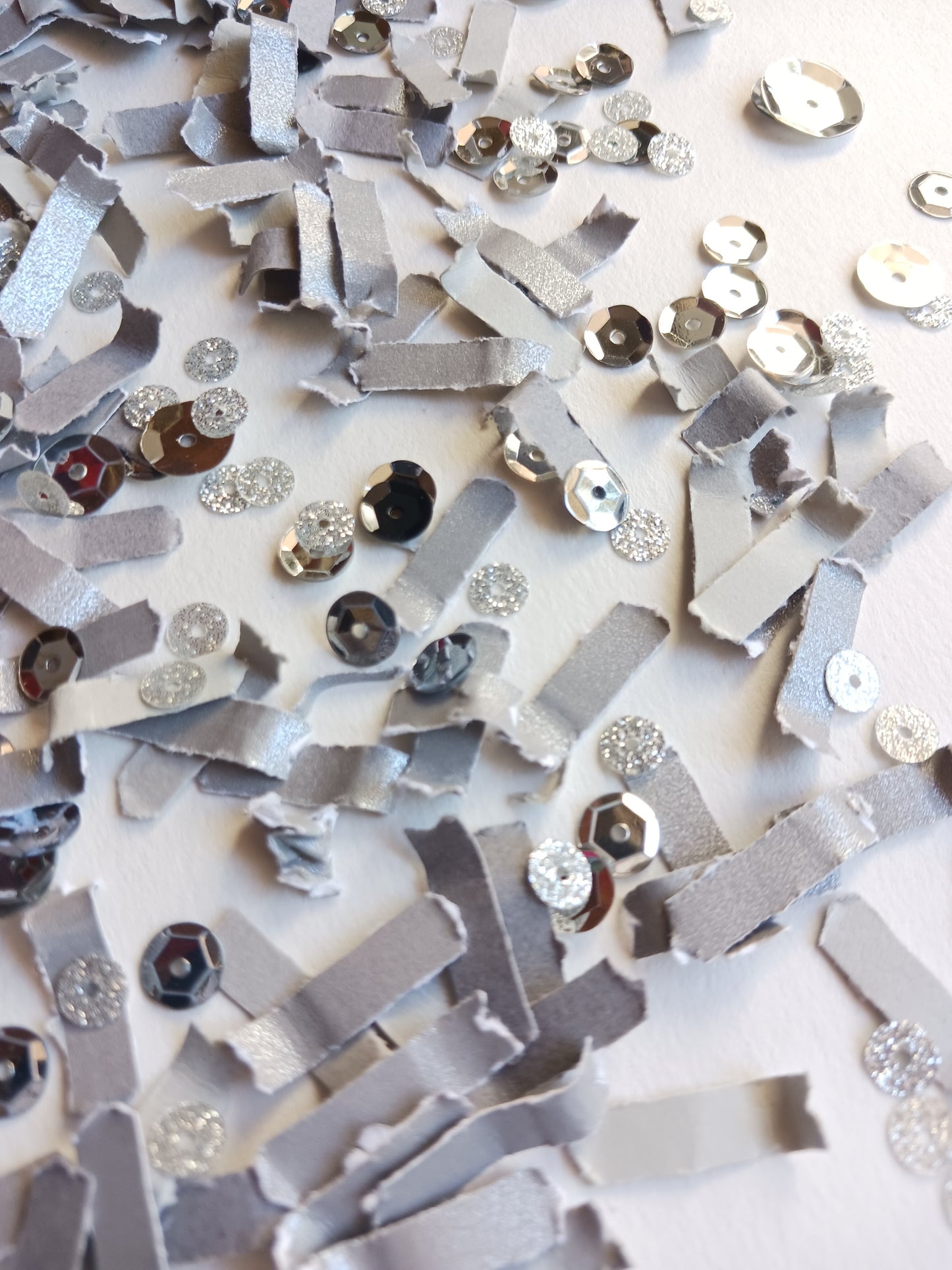 Silver grey confetti with silver glittery sequins on white background. 