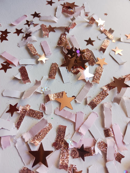 Star-shaped confetti in rose gold, pink, and white on a light background