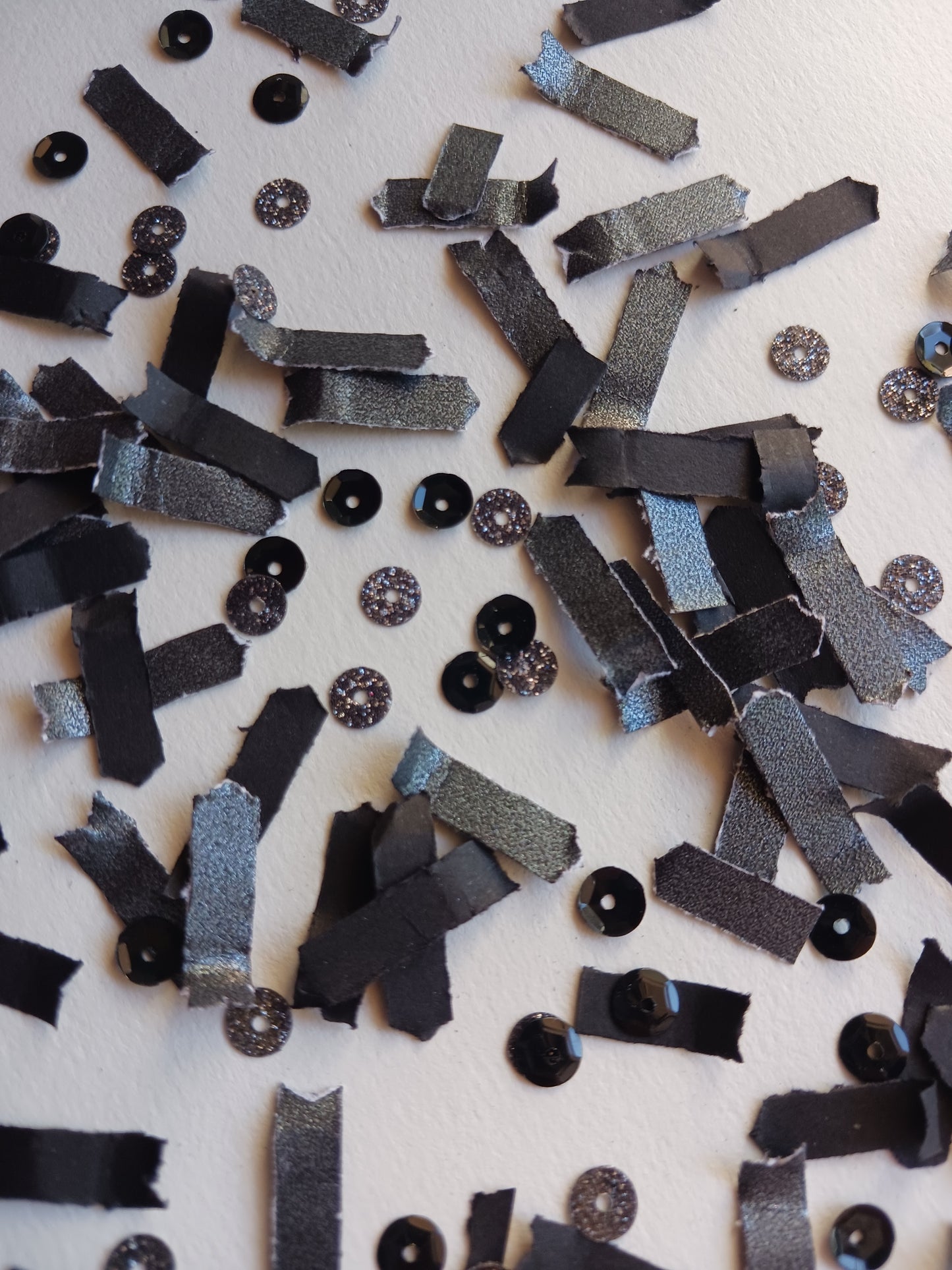 Scattered black paper confetti with glittery sequins on a background. 