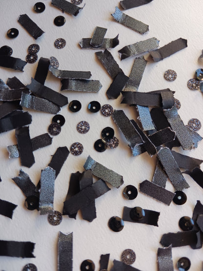 Scattered black paper confetti with glittery sequins on a background. 