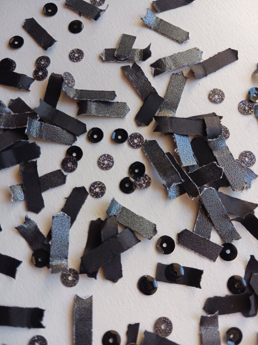 Scattered black paper confetti with glittery sequins on a background. 