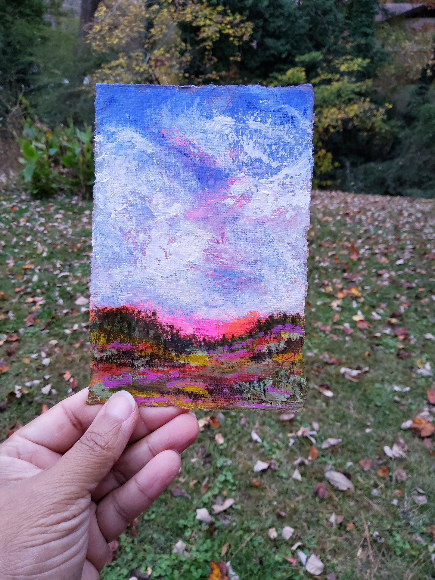 Hand holding a small abstract painting with a colorful gradient against a natural background.