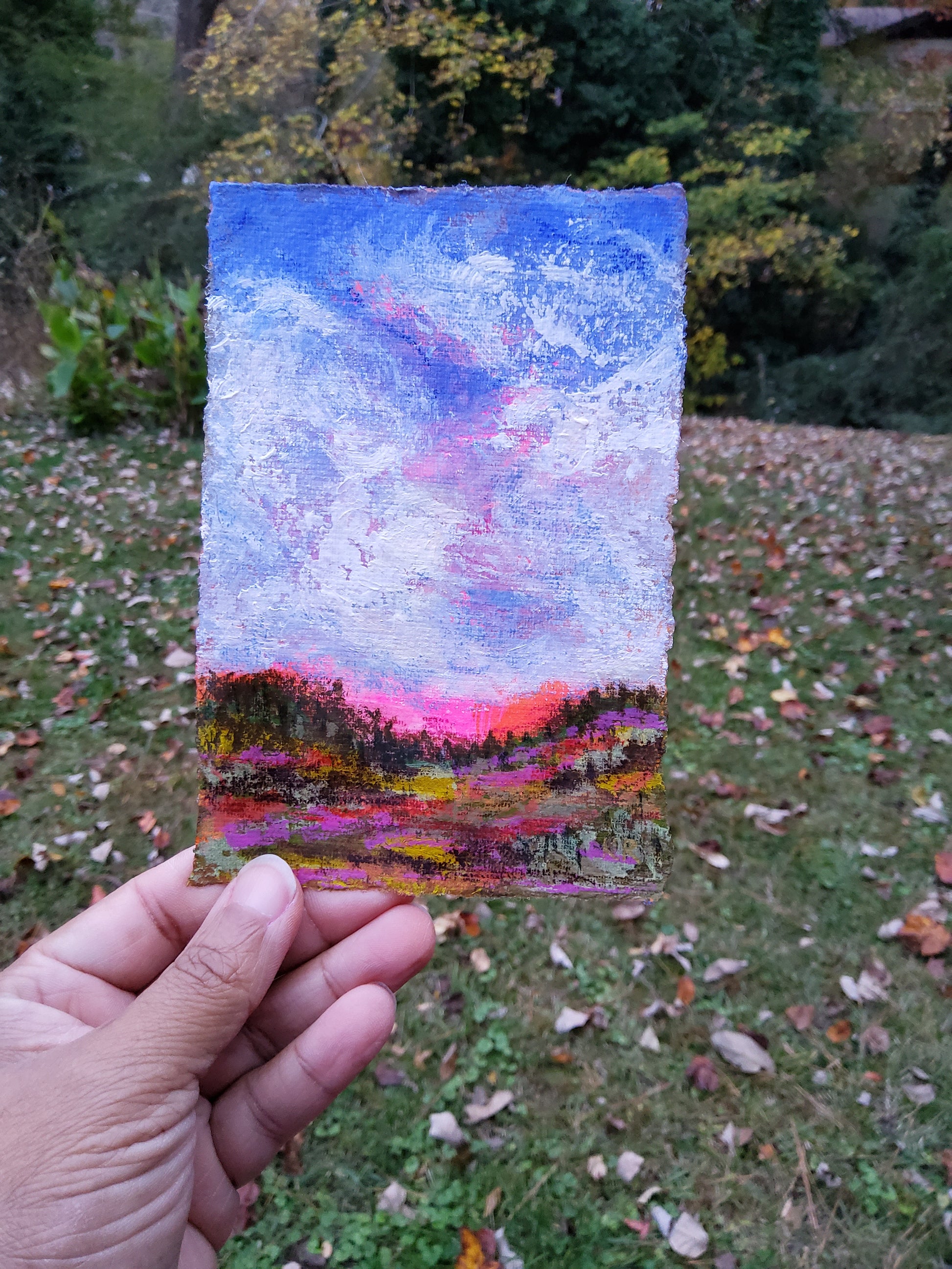 Hand holding a small abstract painting with a colorful gradient against a natural background.