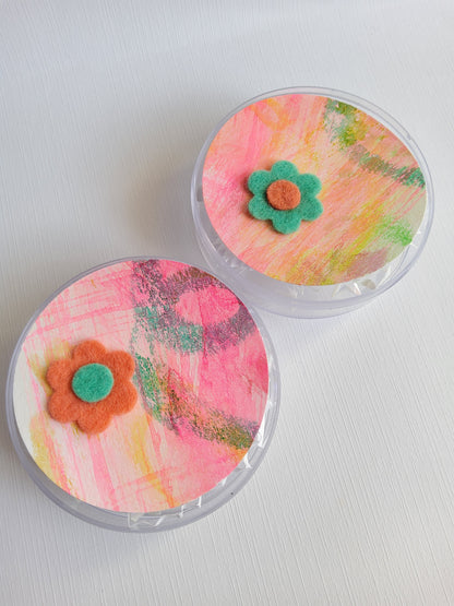 Colorful flower-shaped pins in roun containers on a white background 