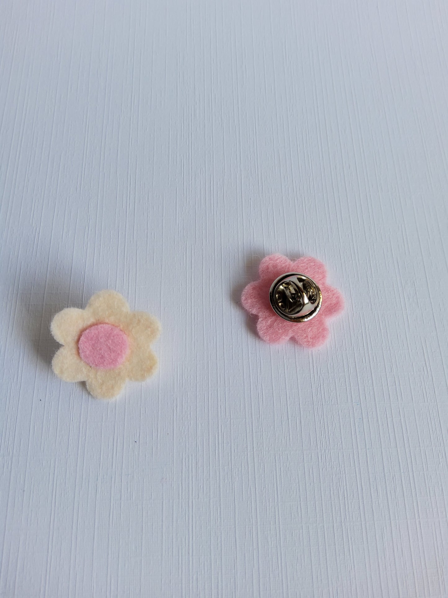 Two flower-shaped pins on a light textured background