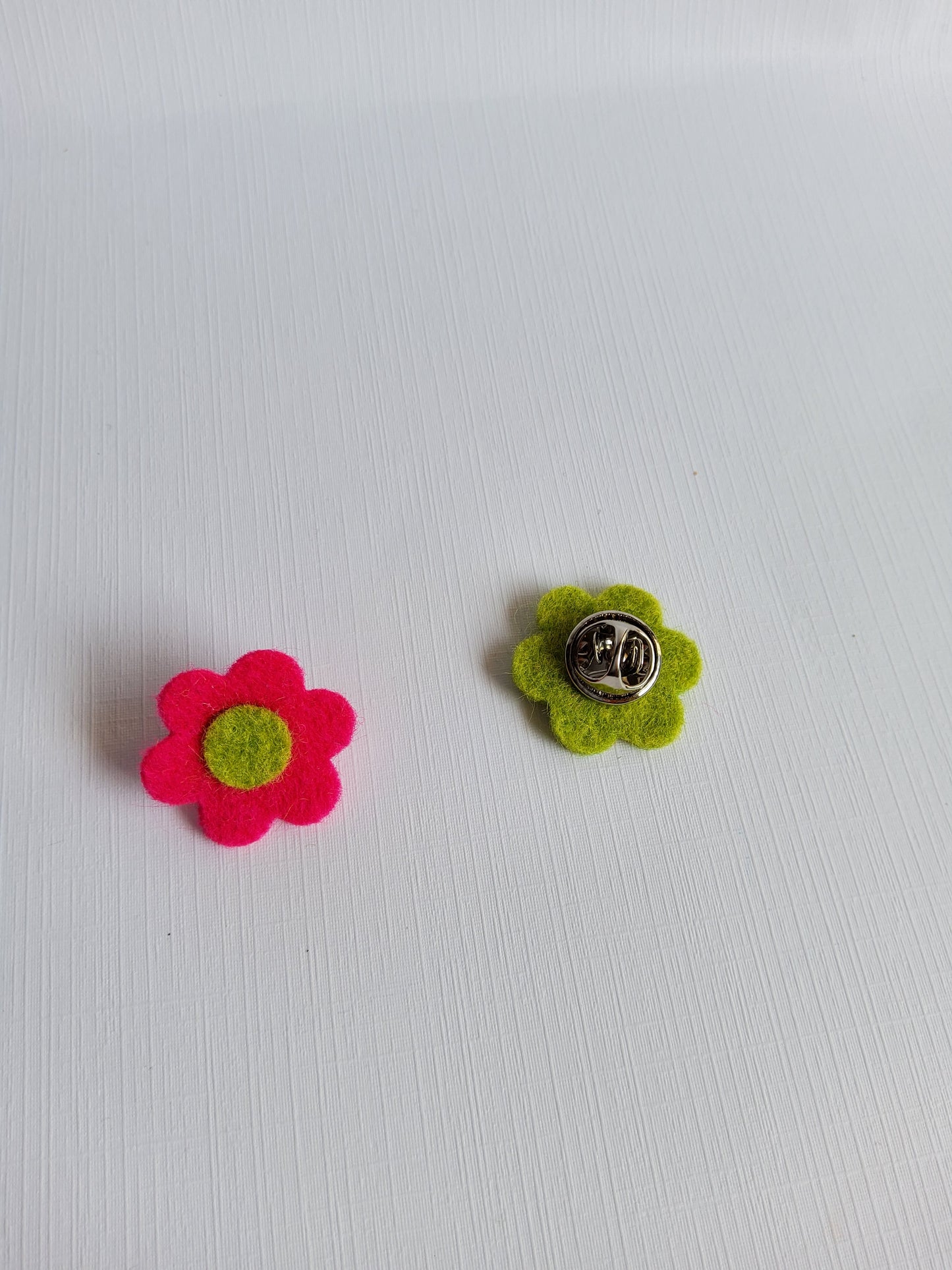 Two felt flower pins, one green and one pink, on a white background.