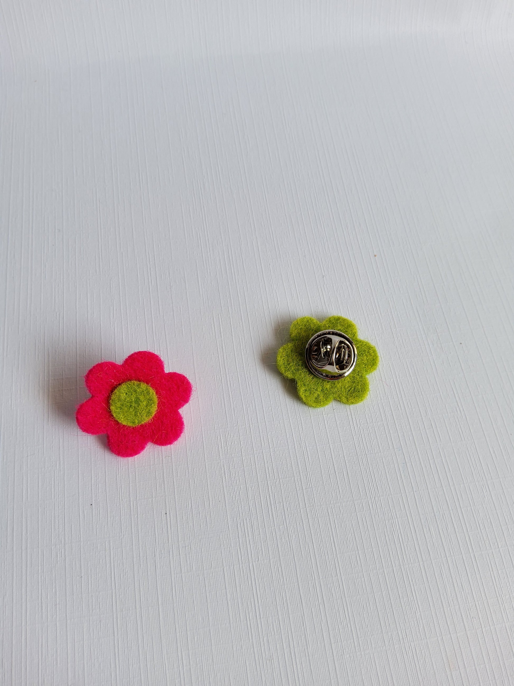 Two felt flower pins, one green and one pink, on a white background.