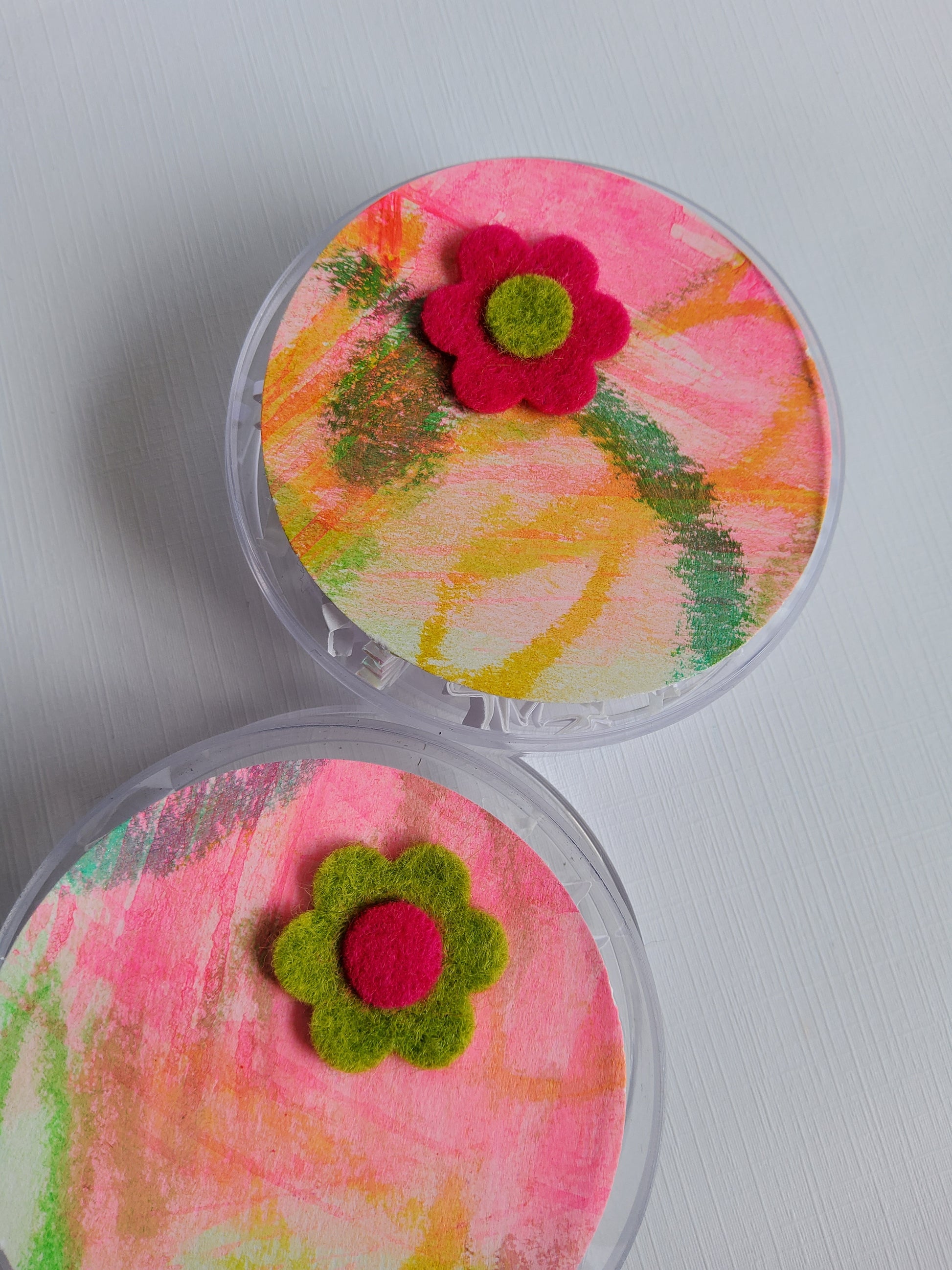 Two small round containers with colorful floral designs on a light gray background