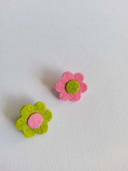 Two felt flower pins, one pink with a green center and one green with a pink center, on a light gray background.