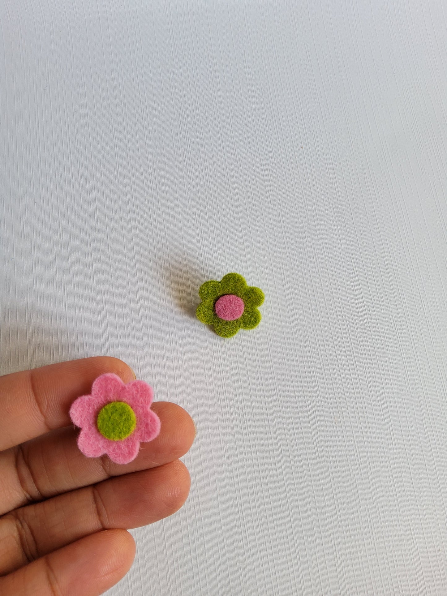 Small pink and green felt flowers on a white background with a hand holding one flower.