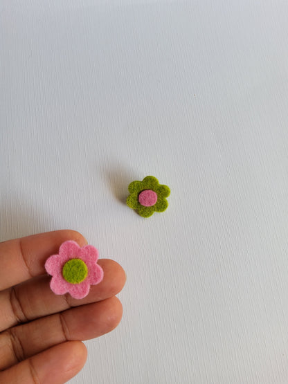 Small pink and green felt flowers on a white background with a hand holding one flower.