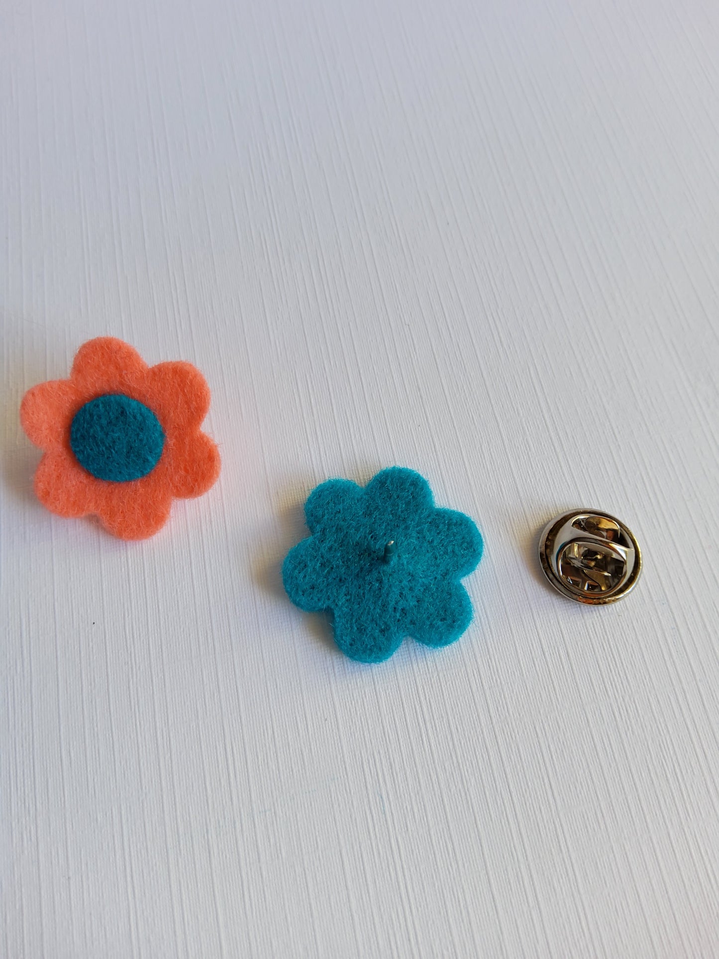Two felt flower pins, one blue and one orange with a blue center, on a white background.