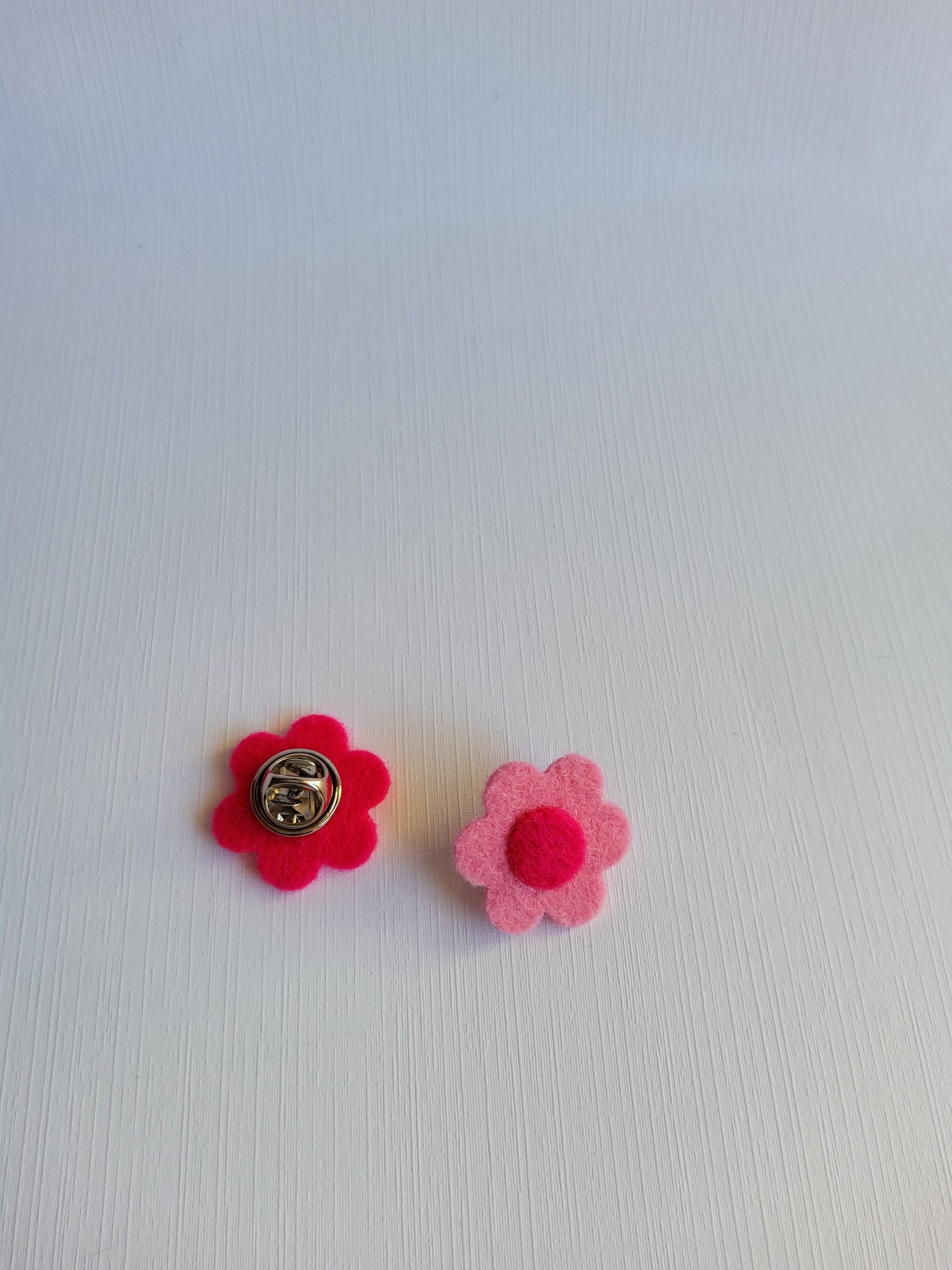 Two pink flower-shaped pins with dot centers on a textured white background
