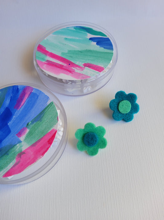 Two colorful containers with abstract designs and two  felt flowers on a white background.