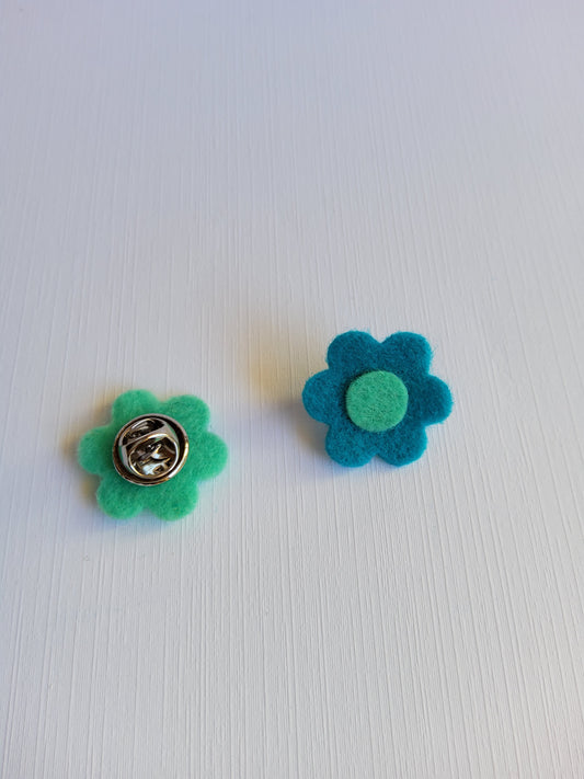 Two felt flower pins, one blue and one green, on a white background.