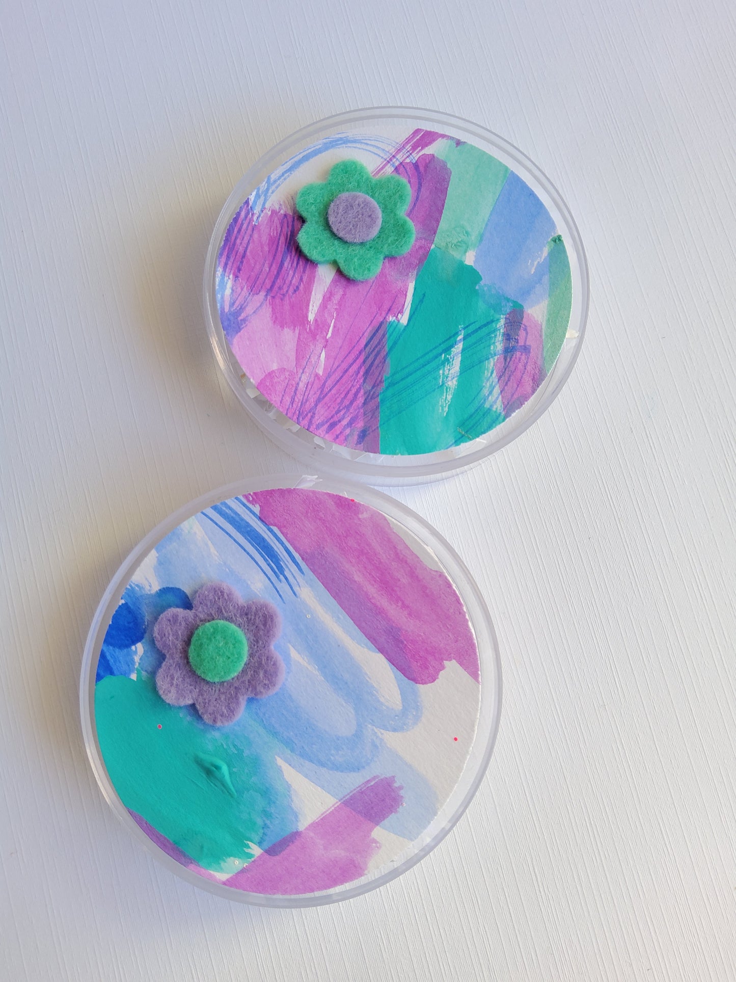Two round containers with colorful paint designs and small flowers on a white background