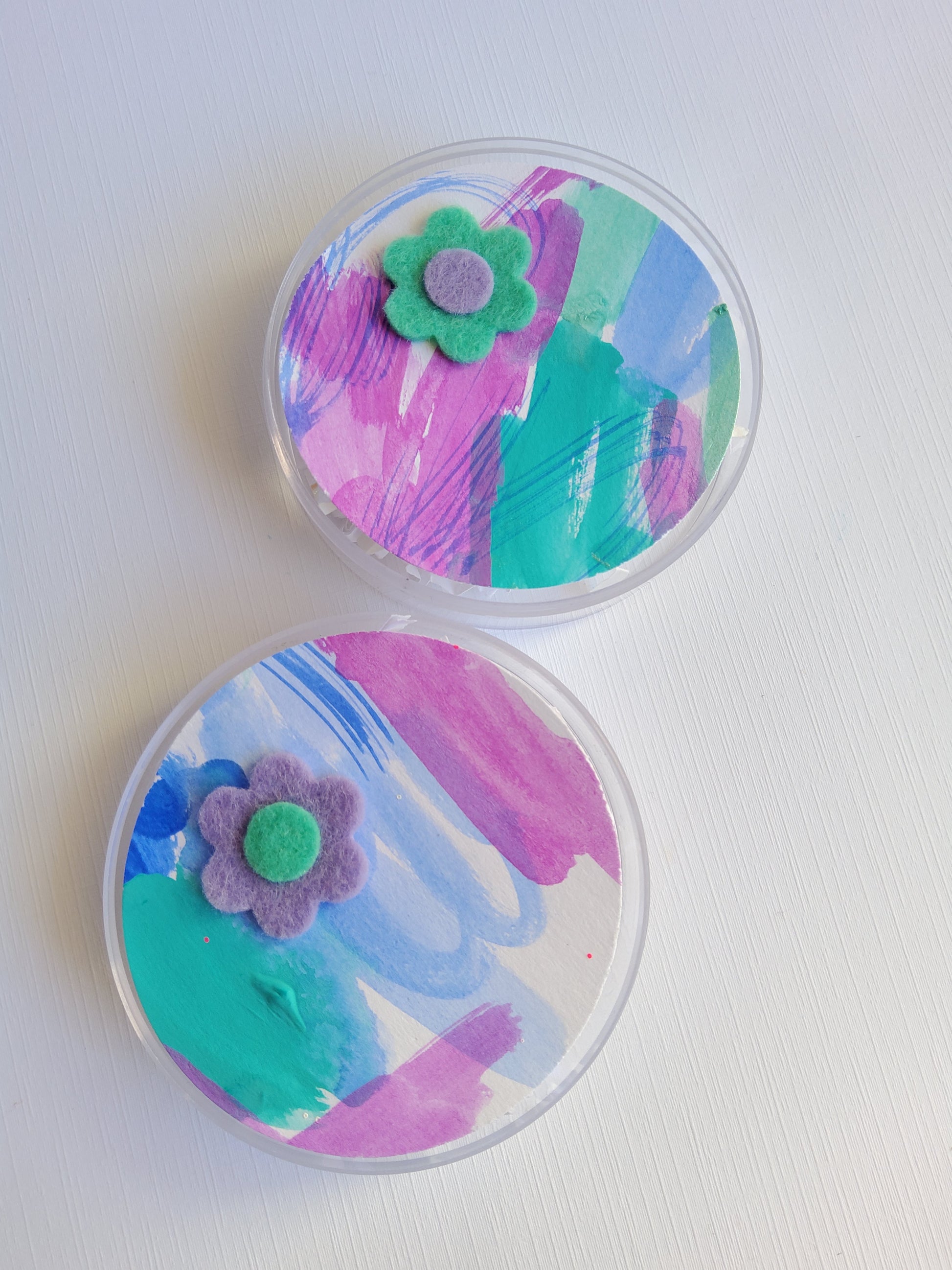 Two round containers with colorful paint designs and small flowers on a white background