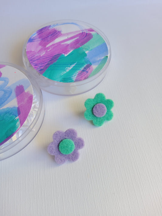 Colorful painted container with two felt flowers on a white background