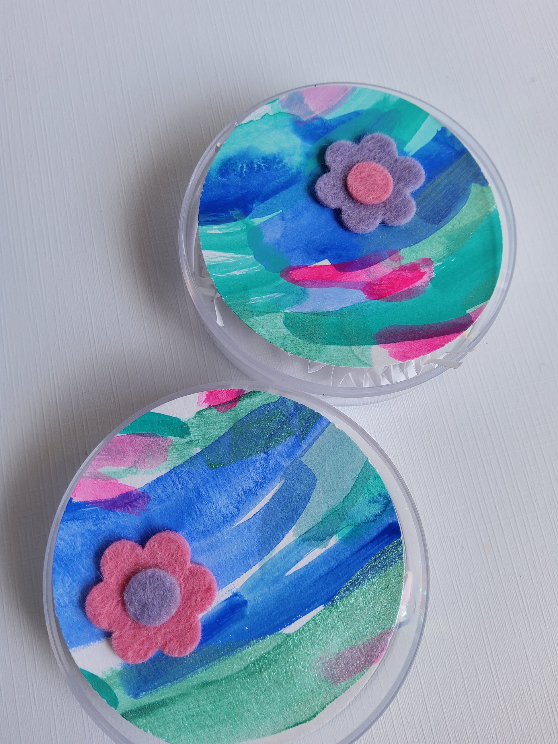 Two round containers with colorful abstract designs and pink flowers on a light gray background