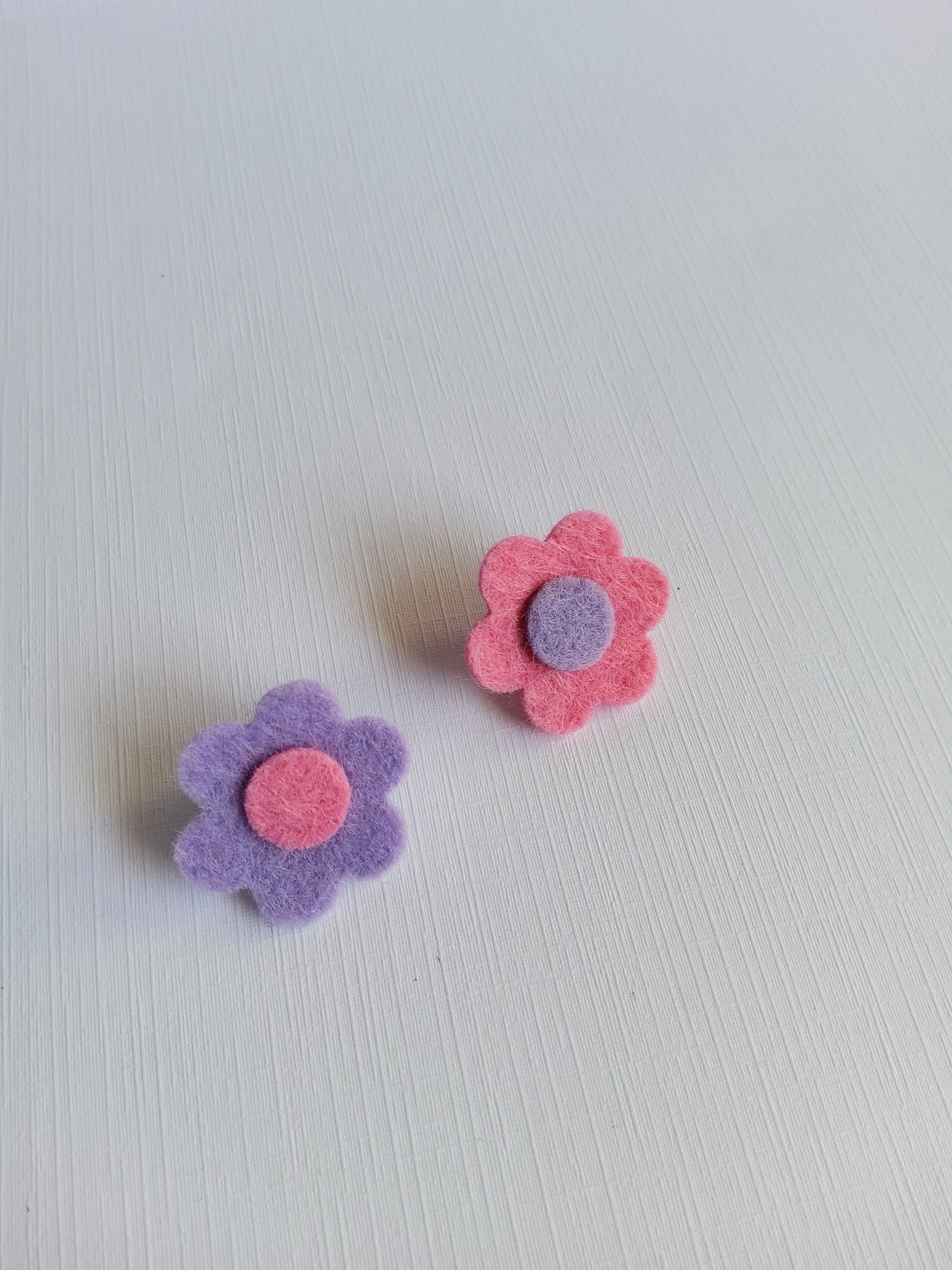 Two felt flowers, one pink and one purple, on a light gray background.