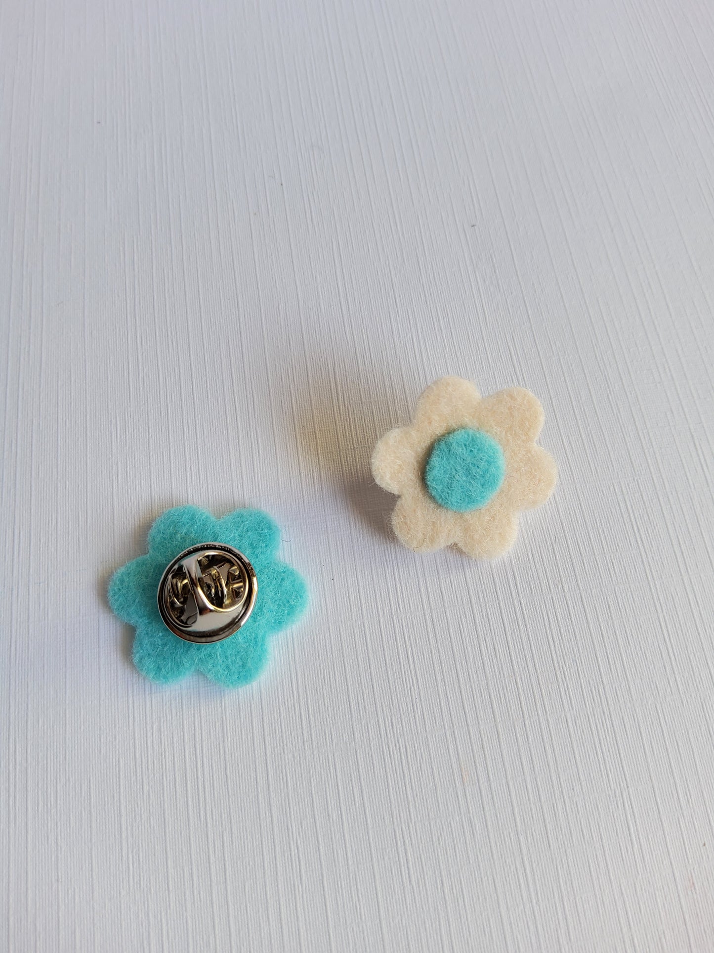 Two felt flower pins on a textured white background
