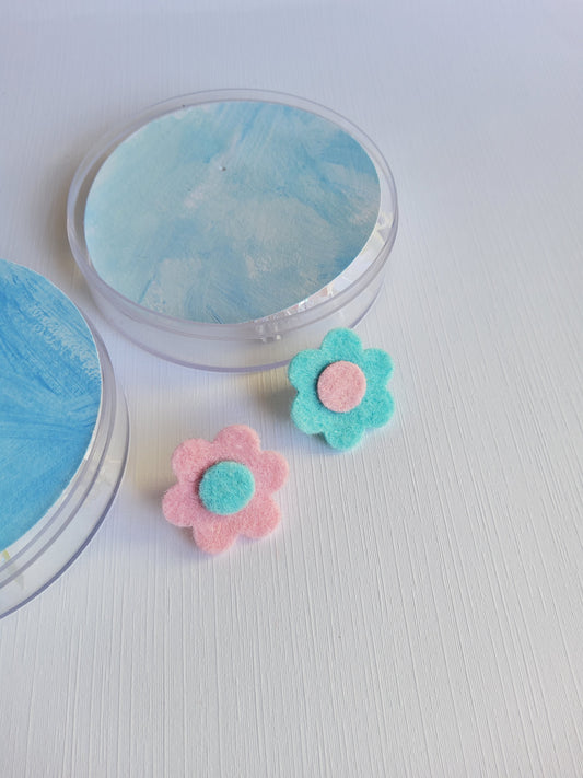 Two small floral lapel pins with pink and blue colors on a light gray background.