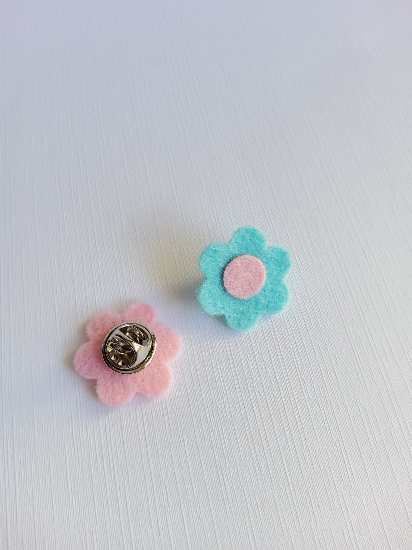 Two flower-shaped pins, one blue and one pink, on a light gray background.