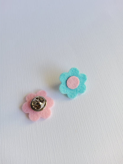 Two flower-shaped pins, one blue and one pink, on a light gray background.