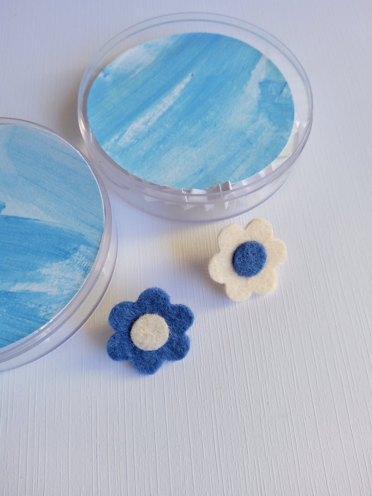 Round acrylic case with two decorative flowers pins on a light gray background
