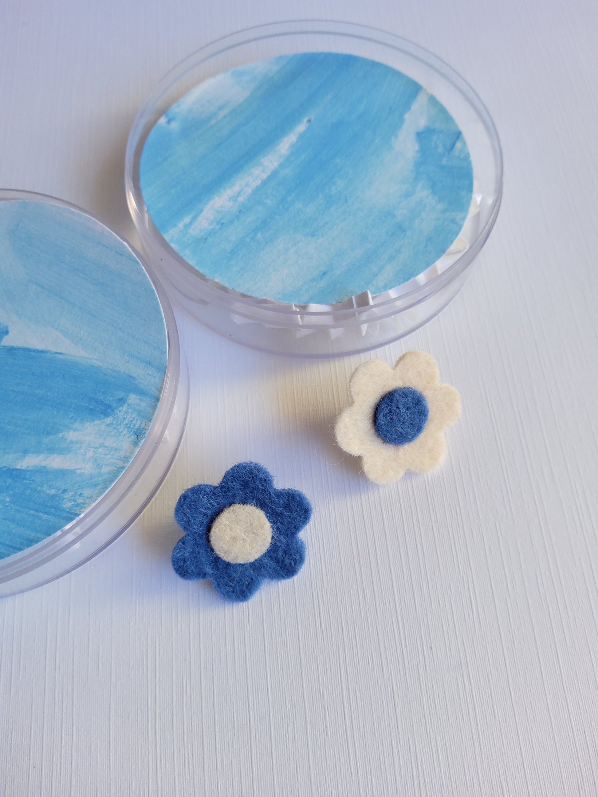 Round acrylic case with two decorative flowers pins on a light gray background