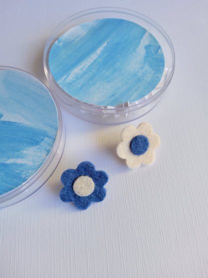 Round acrylic case with two decorative flowers pins on a light gray background