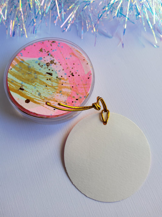 Pink, green and gold accented abstract hand-painted round gift tags with gold cords and blank backing on white background with iridescent tinsel 