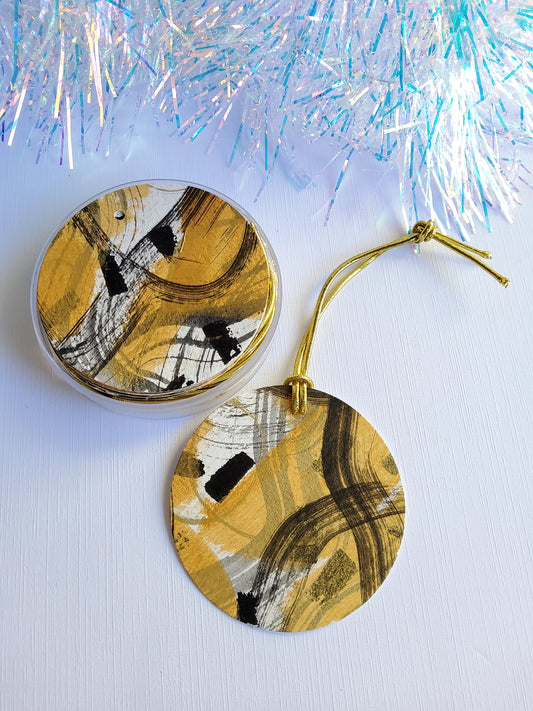 Black and gold abstract hand-painted round gift tags with gold cords in clear round acrylic containers and iridescent tinsel background
