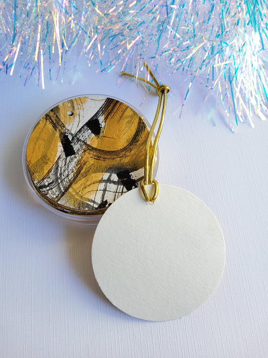 Black and gold abstract hand-painted round gift tags with gold cords and blank side facing up with iridescent tinsel background