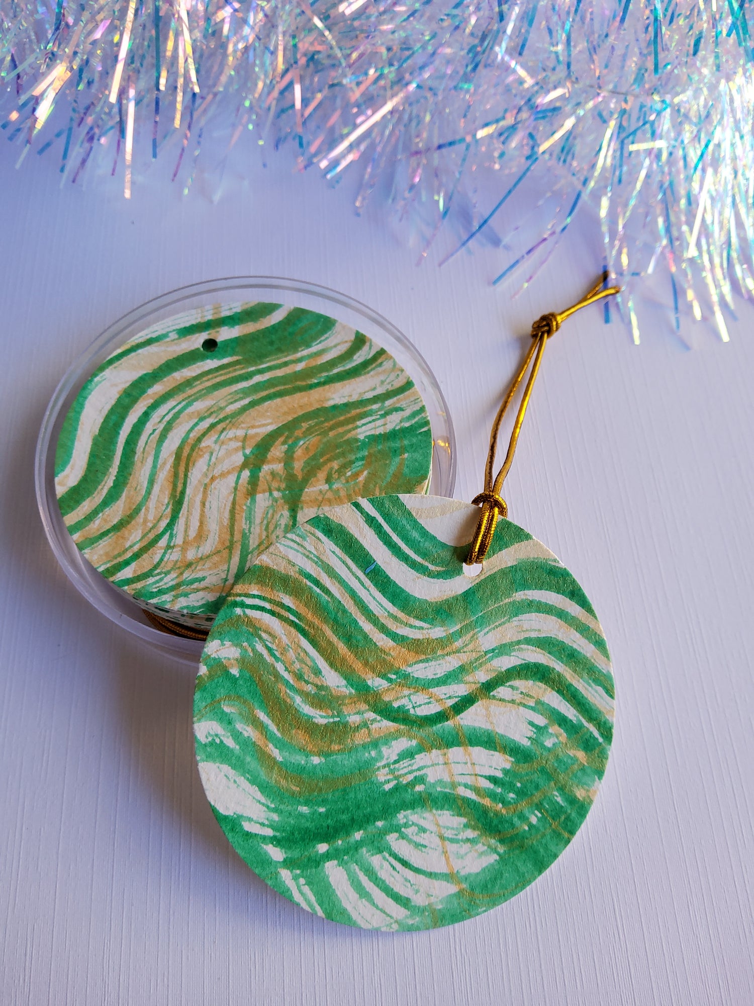 Green abstract hand-painted round gift tags with gold cords and iridescent tinsel background