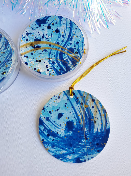 Blue and gold abstract hand-painted round gift tags with gold cords packaged in a clear round acrylic container and iridescent tinsel background