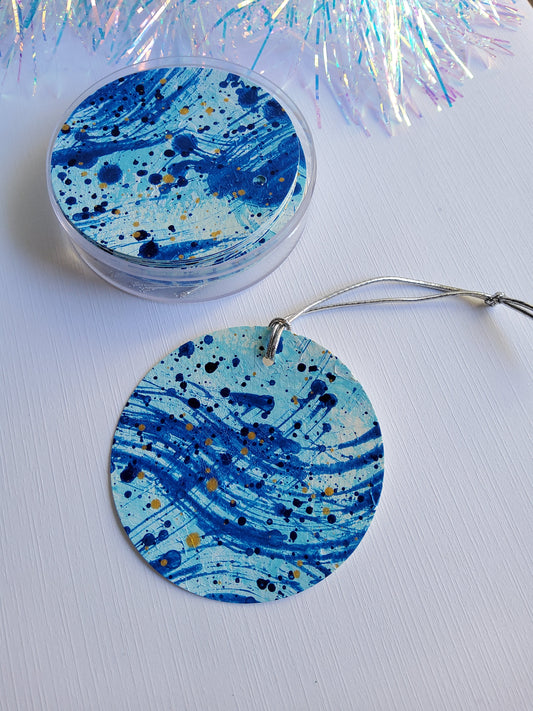 Mixed blues and gold abstract hand-painted round gift tags with silver stretch cords  in clear acrylic container with iridescent tinsel background