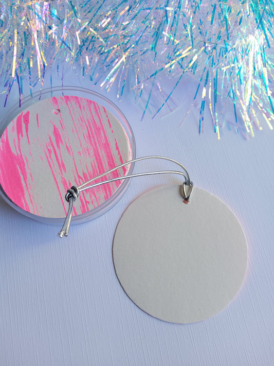 Front and blank back of hand-painted neon pink abstract gift tags with silver stretch cords on white background near iridescent tinsel