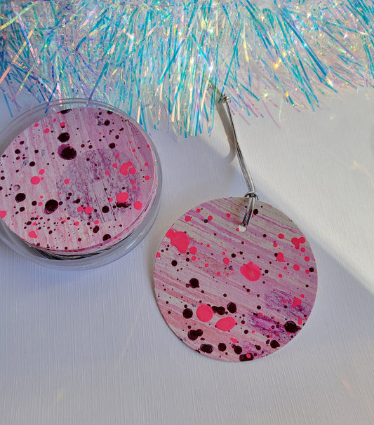 Purple & neon pink abstract hand-painted round gift tags with silver cords in a clear round acrylic container beside iridescent tinsel on a white background