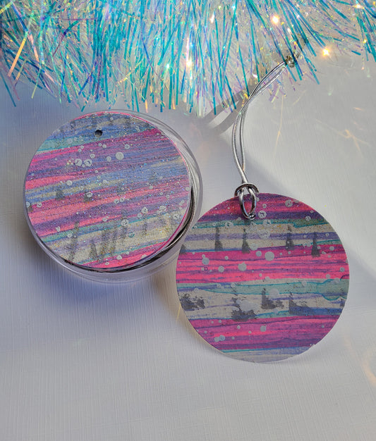 White, silver & neon pink abstract hand-painted round gift tags with silver cords in a clear round acrylic container beside iridescent tinsel on a white background