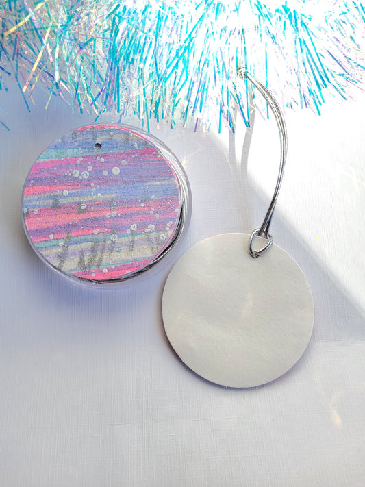 Silver,  lavender & pink abstract hand-painted round gift tags with silver cords in a clear round acrylic container beside iridescent tinsel on a white background