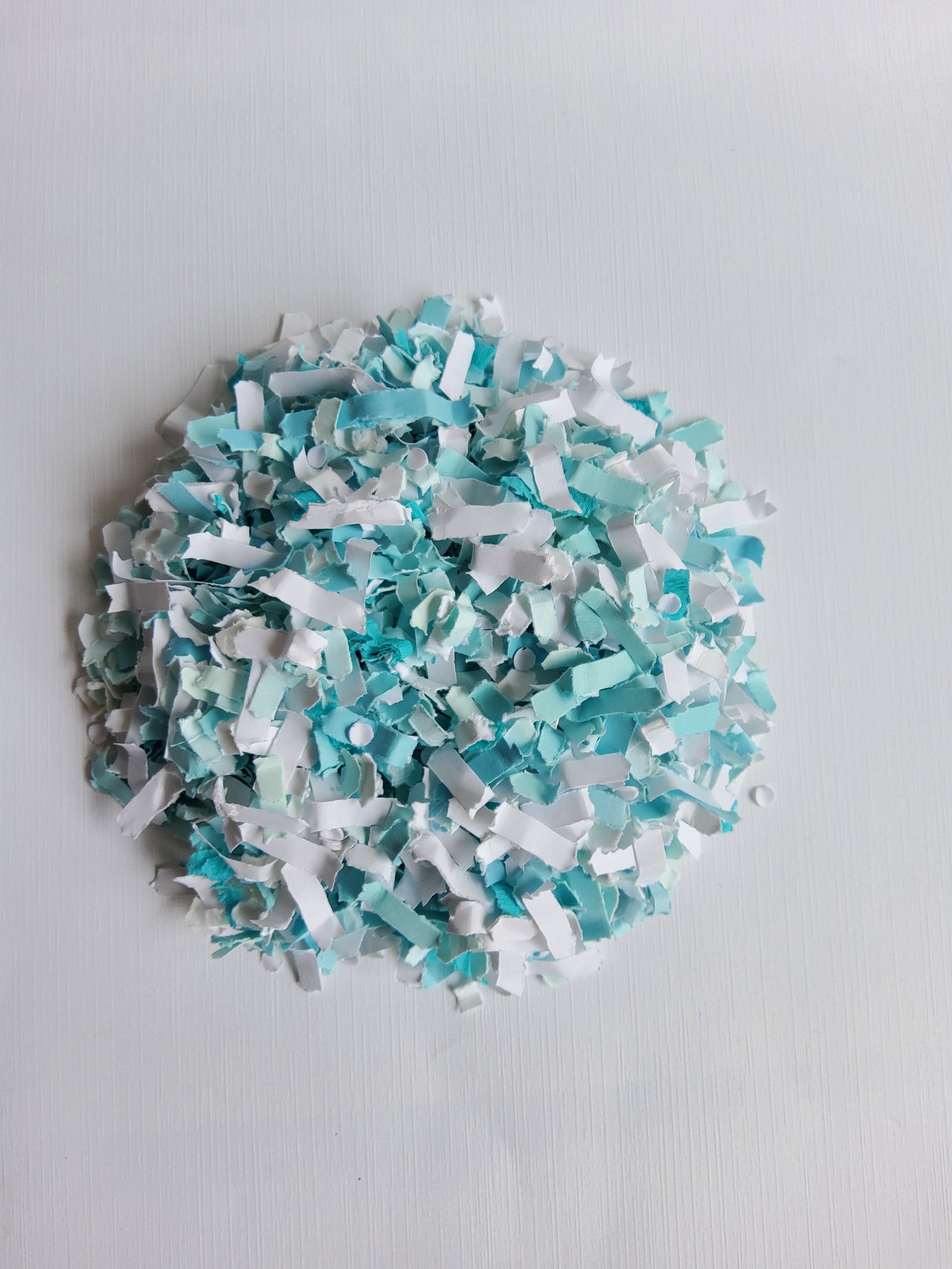 Turquoise and white paper confetti pile on white background. 