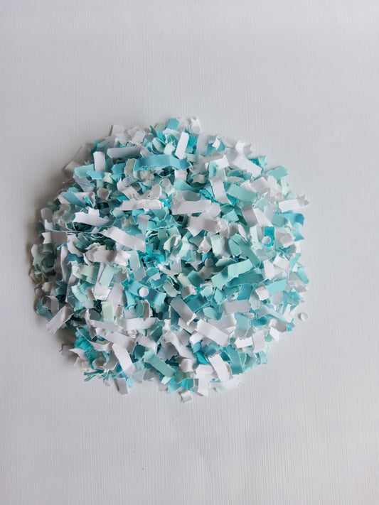 Turquoise and white paper confetti pile on white background. 